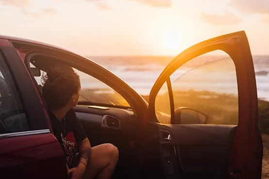 Passager assis dans une voiture ouverte face à la mer au coucher du soleil