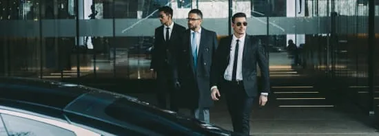 Trois hommes en costume près d’une berline devant des bureaux
