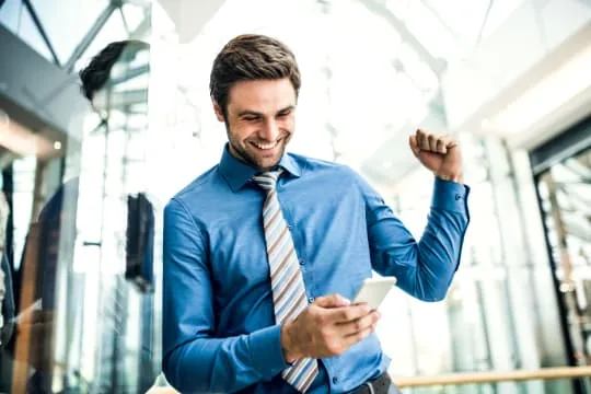 Homme souriant en chemise bleue utilisant son téléphone dans un hall lumineux