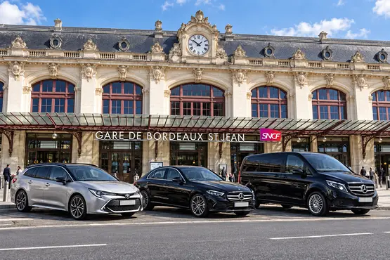 Deux berlines et un van devant la façade de la gare de Bordeaux Saint-Jean.