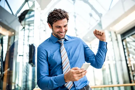 Homme souriant en chemise bleue utilisant son téléphone dans un hall lumineux